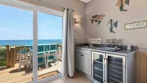 A kitchen with a view of the ocean, a deck with chairs and a table, and decorative wall art.