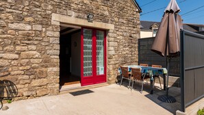 A stone building with a red door, a table with chairs, and an umbrella. - Non-air-conditioned country cottage near a farm (Questembert)