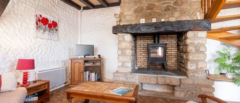 A cozy living room with a stone fireplace, a television, and a bookshelf.