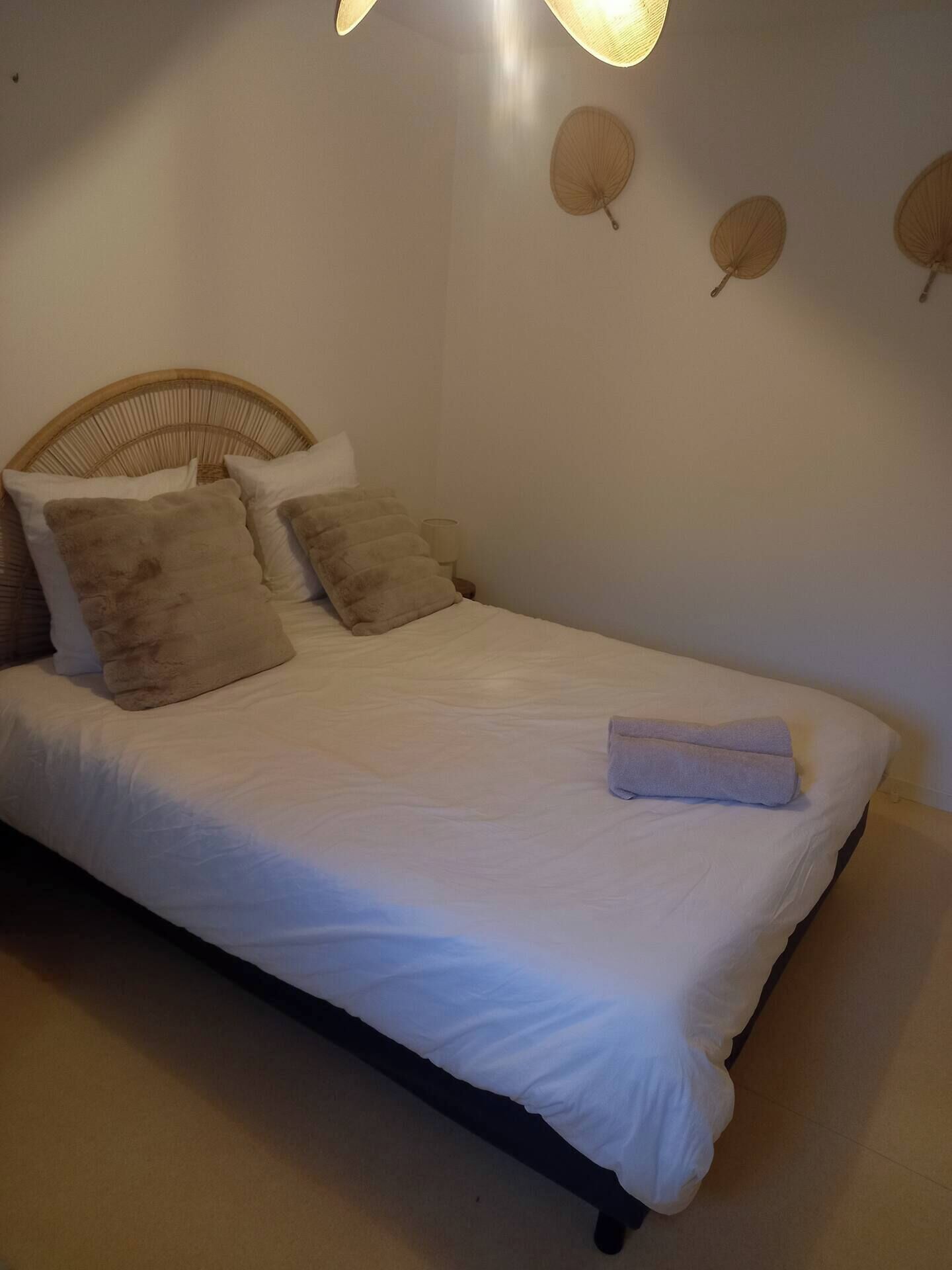 A neatly made bed with white linens and a folded towel, a wicker headboard, and wall-mounted decorative leaves.