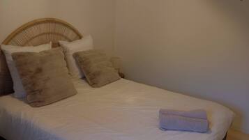 A neatly made bed with white linens and a folded towel, a wicker headboard, and wall-mounted decorative leaves.