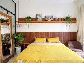 Ein Hotelzimmer mit Bett, Sessel, Spiegel und Regal mit Pflanzen und Bildern.