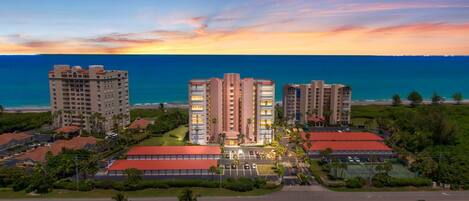 A high-rise hotel with multiple floors, a parking lot, and a view of the ocean at sunset.