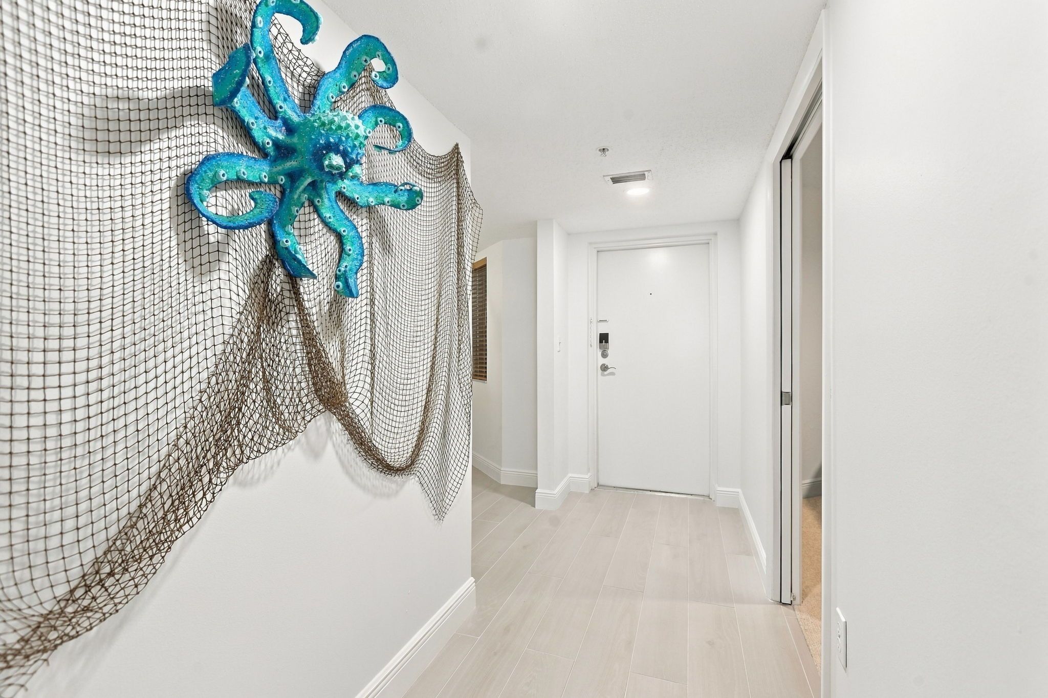 A hallway with a white door at the end, a textured wall decoration, and a light-colored floor.