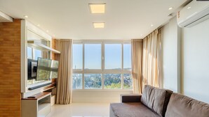 A modern living room with a large window, a flat-screen TV, and a sofa.