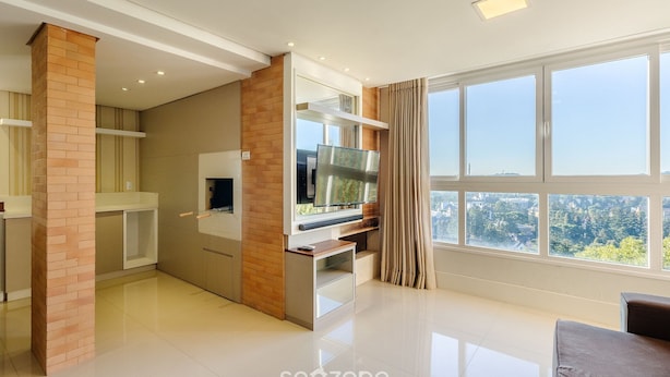 A modern kitchen with a built-in oven, a large window with curtains, and a flat-screen TV mounted above the counter.