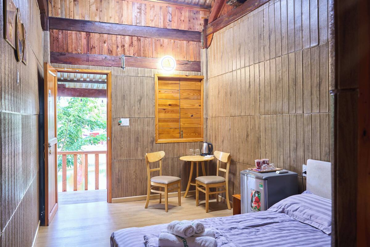 A wooden cabin room with a bed, two chairs, a small table, and a kitchenette.