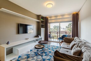 A modern living room with a flat-screen TV mounted on the wall, a sofa, a coffee table, and a patterned rug. - Beautiful Apartment With Heated Pool Cap0302 (Gramado)