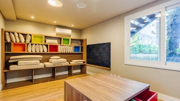 Una habitación moderna con suelo de madera, una mesa de madera y una ventana con vistas a zonas verdes. Se observan estanterías con almohadas y cajas de almacenamiento.