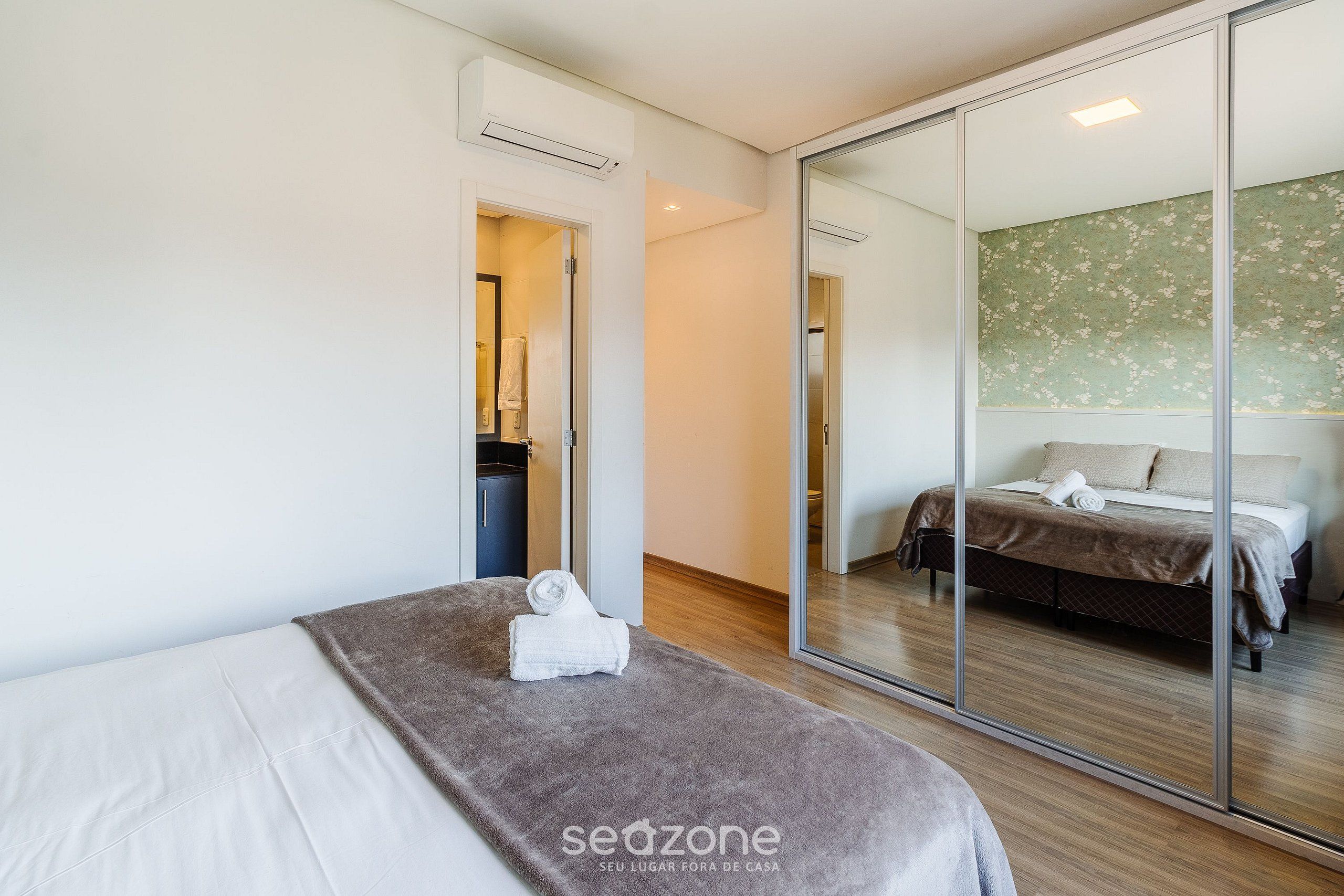 A modern hotel room with a large bed, a separate seating area, and a mirrored wall reflecting the bedroom.