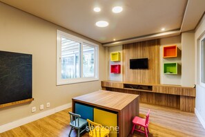 A modern children's playroom with a wooden table, colorful chairs, a chalkboard, and built-in shelves. - Beautiful Apartment With Heated Pool Cap0302 (Gramado)