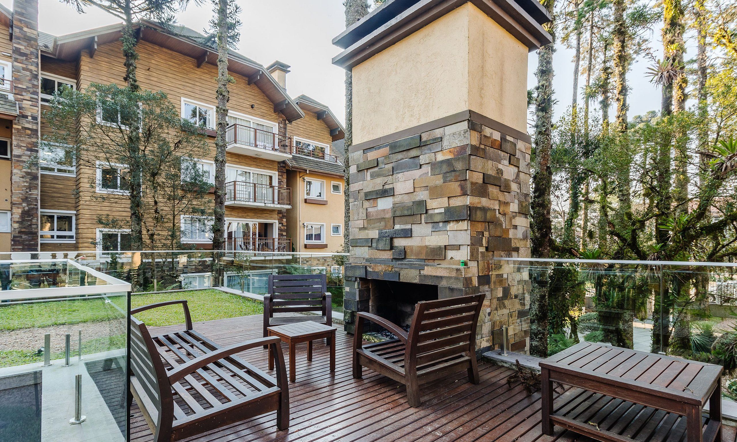A wooden deck with outdoor furniture, a stone fireplace, and a view of a multi-story building with balconies.