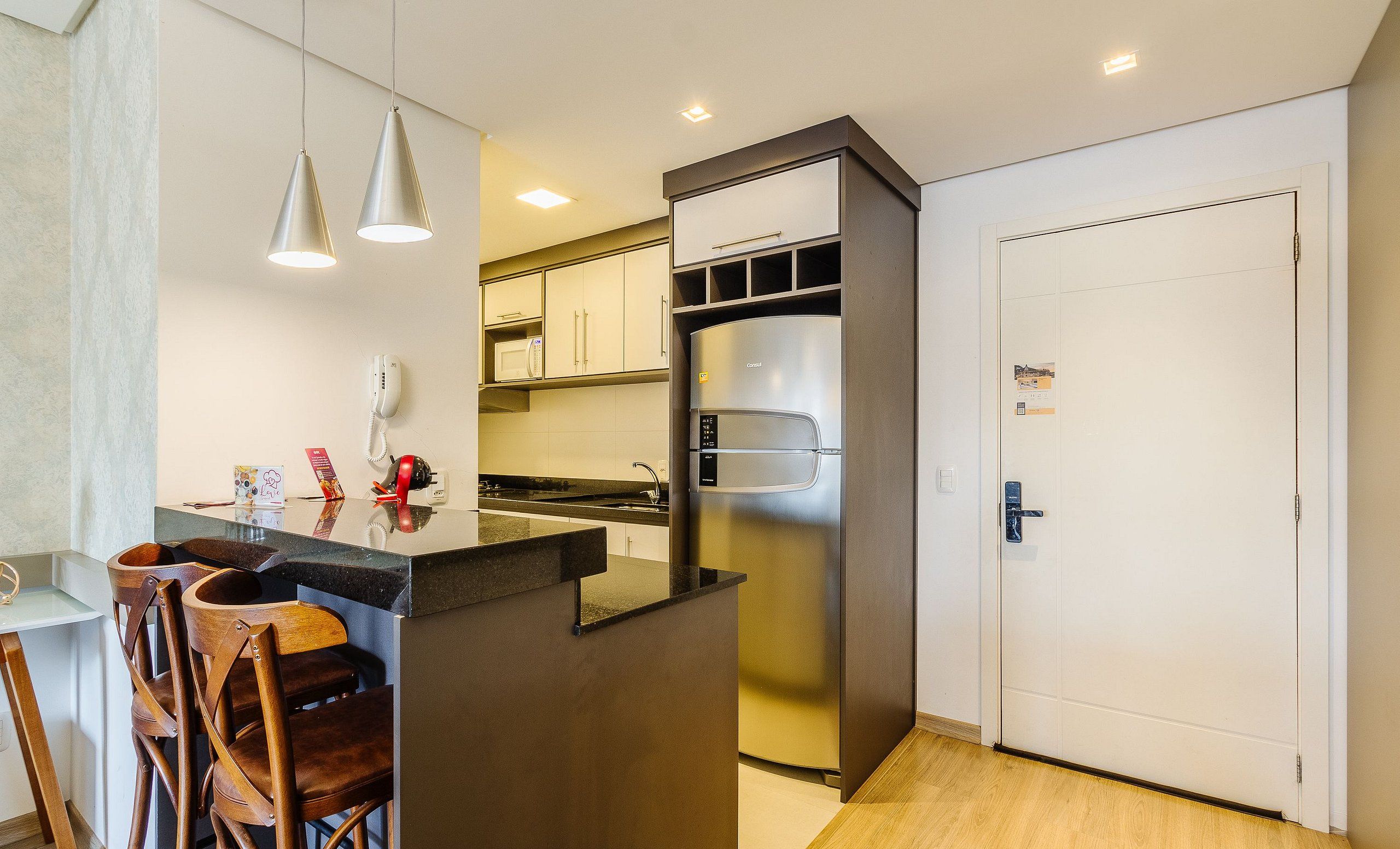 Una cocina compacta con un refrigerador integrado, un microondas y una cafetera. Hay una pequeña barra con taburetes y un teléfono en la pared.