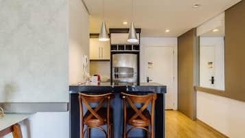 Una cocina moderna con una isla central, dos taburetes de madera, iluminación colgante y un refrigerador de acero inoxidable.