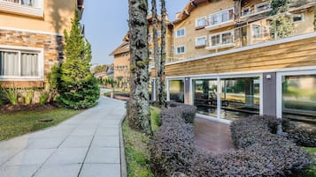 A modern residential building with a paved pathway, neatly trimmed hedges, and a small water feature.