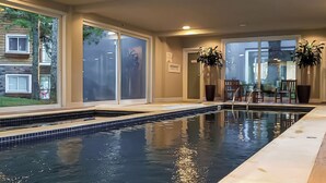 Una piscina interior con paredes de vidrio transparente, suelo de baldosas y plantas en macetas.