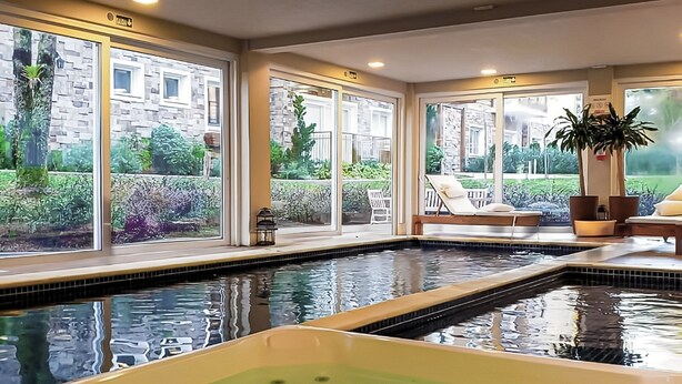 Zona de piscina con jacuzzi, ventanas amplias y mobiliario exterior.