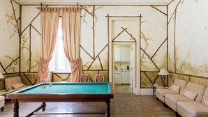 A billiards table in a room with a herringbone-patterned floor, a sofa, and a dining area visible through a doorway. - Royal Hideaway – Estoril 2BR Pool Retreat (Cascais)