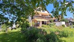 A two-story house with a balcony, surrounded by a well-maintained garden with various plants and flowers. - Large vacation apartment with terrace at the entrance to the northern Black Forest. Quiet residential area (Gaggenau)
