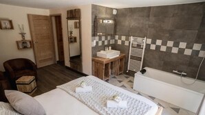 Een hotelkamer met een bed, een houten nachtkastje, een badkamer met een badkuip en een betegelde muur met een geruit patroon.