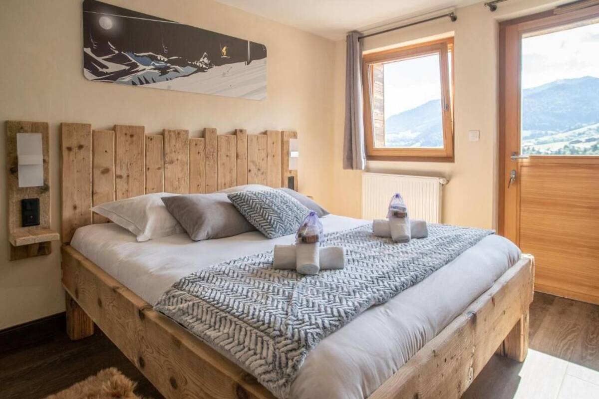 A wooden bed with a herringbone-patterned throw, a nightlight, and a window with a mountain view.