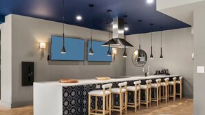 A modern kitchen with a central island, bar stools, pendant lighting, and blue wall art. - Designer 2BR | Gym, Parking (White Plains)