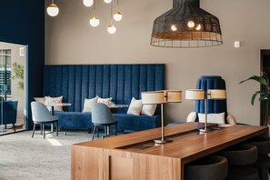 A modern lounge area with a blue upholstered sofa, two armchairs, a wooden coffee table, and a large hanging light fixture. - Designer 2BR | Gym, Parking (White Plains)