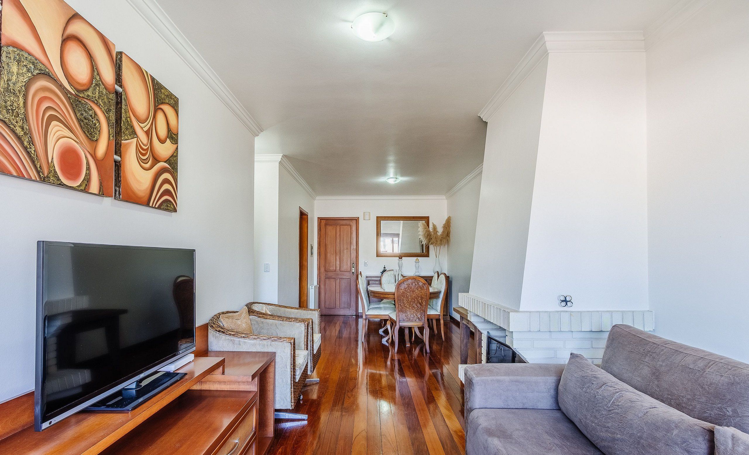 A spacious living room with a flat-screen TV, a gray sofa, and a dining area with chairs and a table.