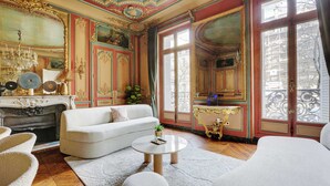 A room with a fireplace, white sofa, round coffee table, and large windows with decorative iron railings.