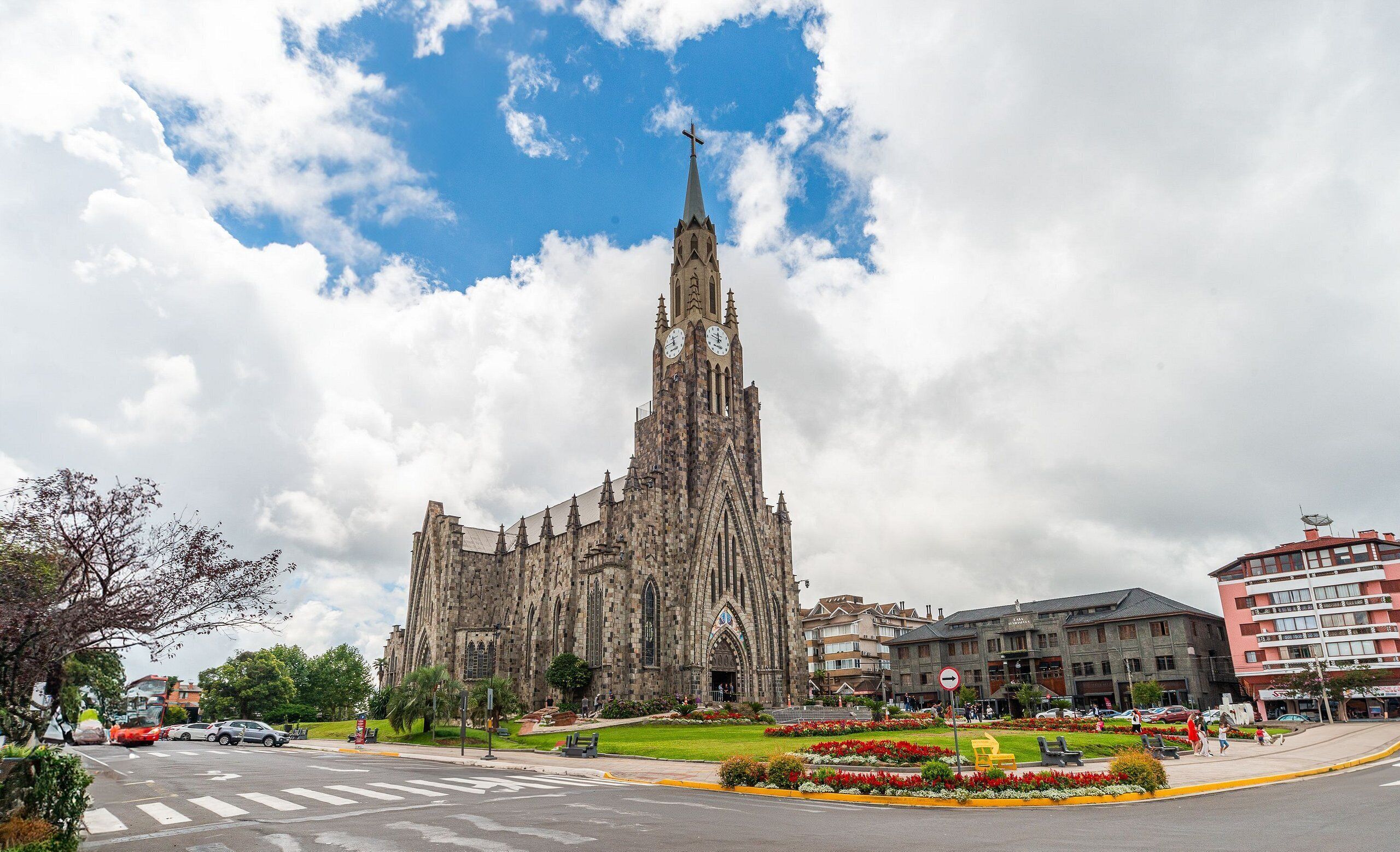 Eine historische Kirche mit einem hohen Turm und einer Turmuhr, umgeben von einem gepflegten Garten und modernen Gebäuden.