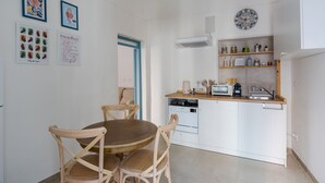 Una cocina compacta con armarios blancos, encimera de madera y lavavajillas integrado. Hay dos sillas de madera alrededor de una mesa redonda.