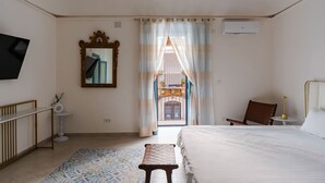 Habitación de hotel con cama, una mesita, una silla, televisor, espejo y vistas al balcón exterior.