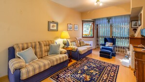 A living room with two sofas, a blue armchair, a patterned rug, and a window with curtains.