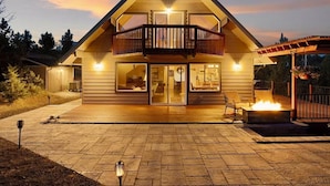 A two-story house with a balcony, a fire pit, and a well-lit entrance.