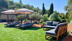 Een terras met lounge fauteuils en parasols, omgeven door groen en stenen muren.