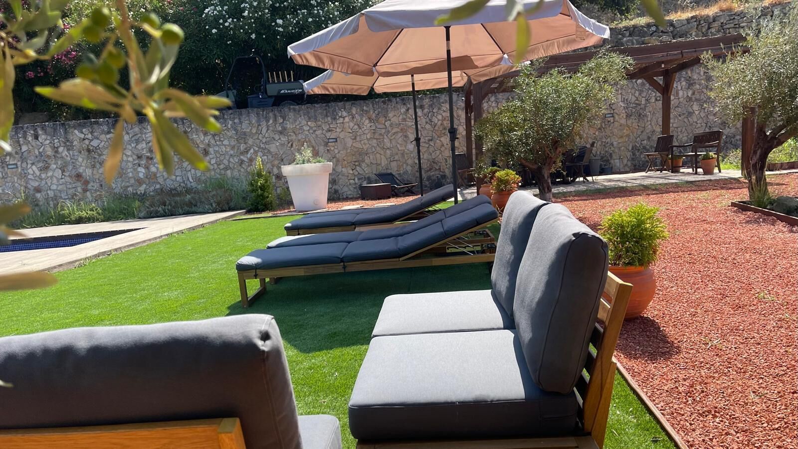 A patio area with outdoor seating, including a sofa and lounge chairs, under a large umbrella.