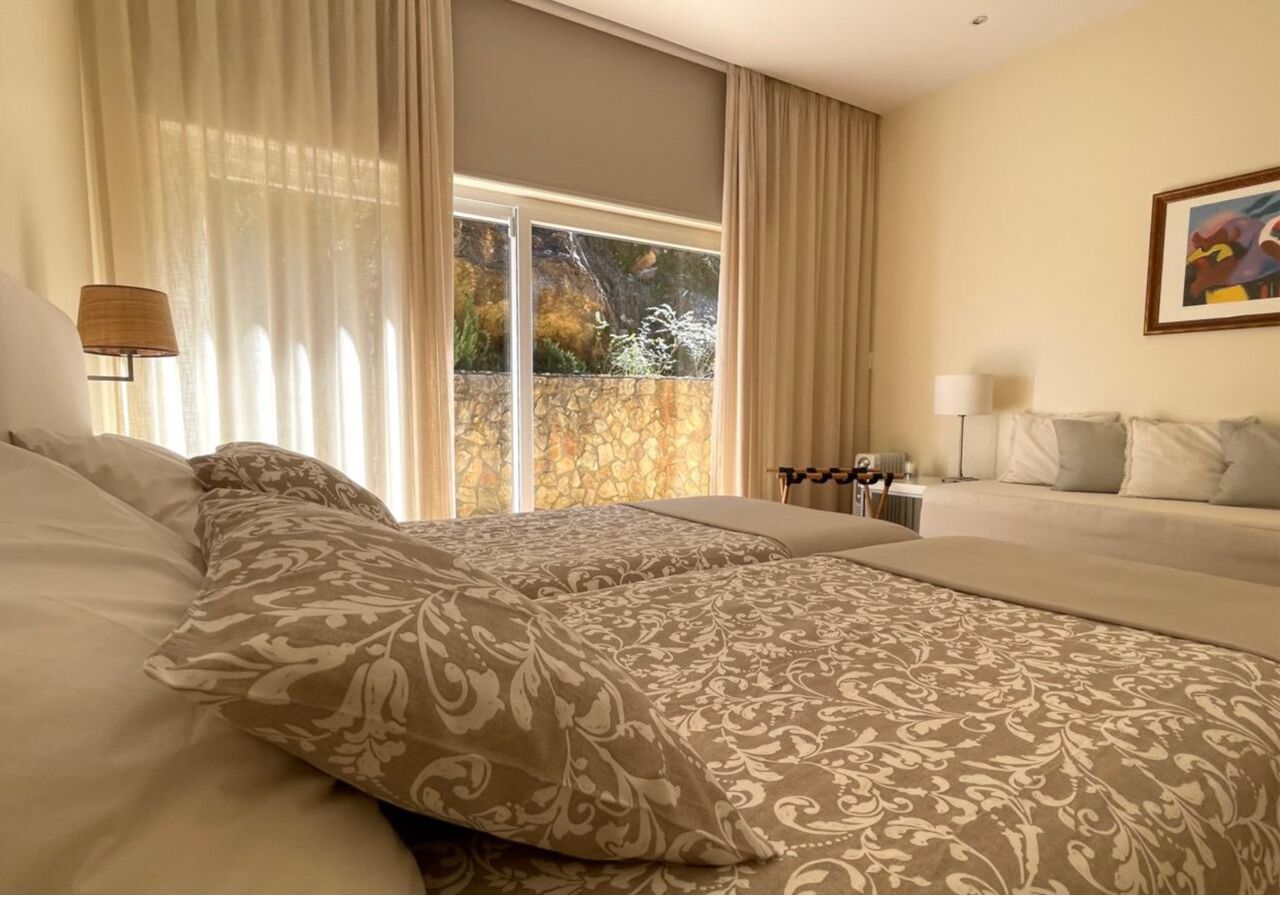 A hotel room with a large bed, a smaller sofa, a window with curtains, and a painting on the wall.