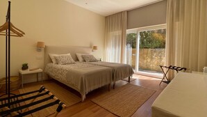Een slaapkamer met een bed, nachtkastjes, een hangstoel en uitzicht op de natuur.