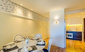 A dining area with a table set for four, chairs, and a kitchen visible in the background.