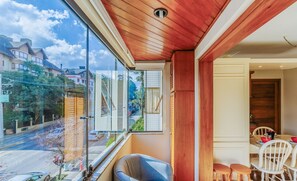 A room with a large window, a wooden ceiling, and a dining area with chairs and a table. - Units in Building With Swimming Pool in Gramado - MDC (Gramado)