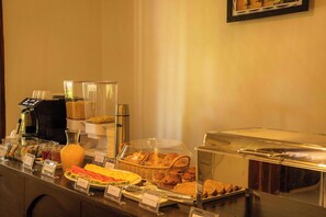 Un bufé con diversas opciones de comida, entre ellas frutas, pasteles y una estación de café.