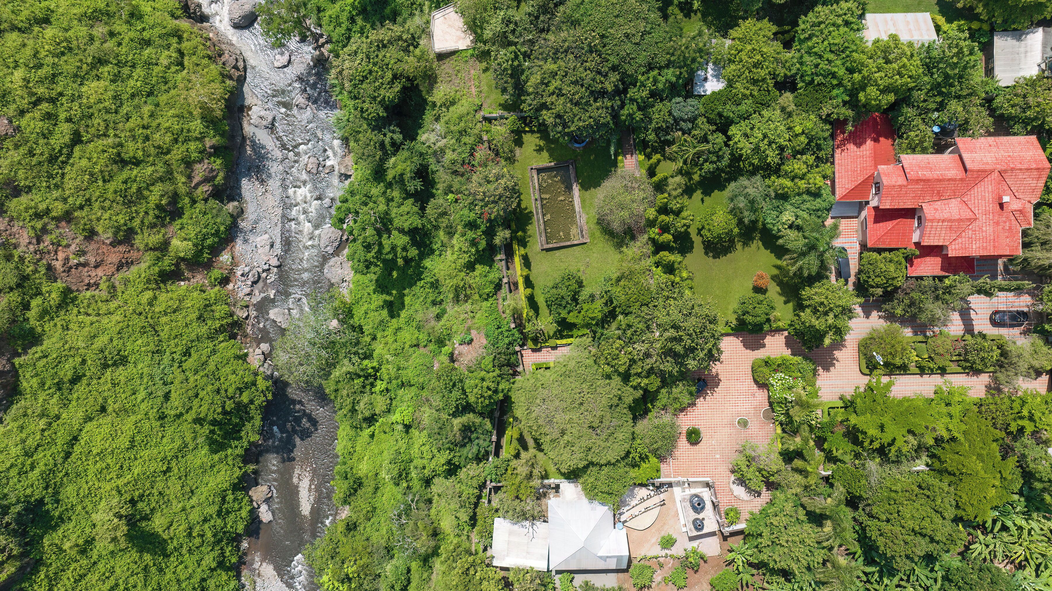 Vista aérea de una zona residencial con un río, abundante vegetación y un edificio de techo rojo.