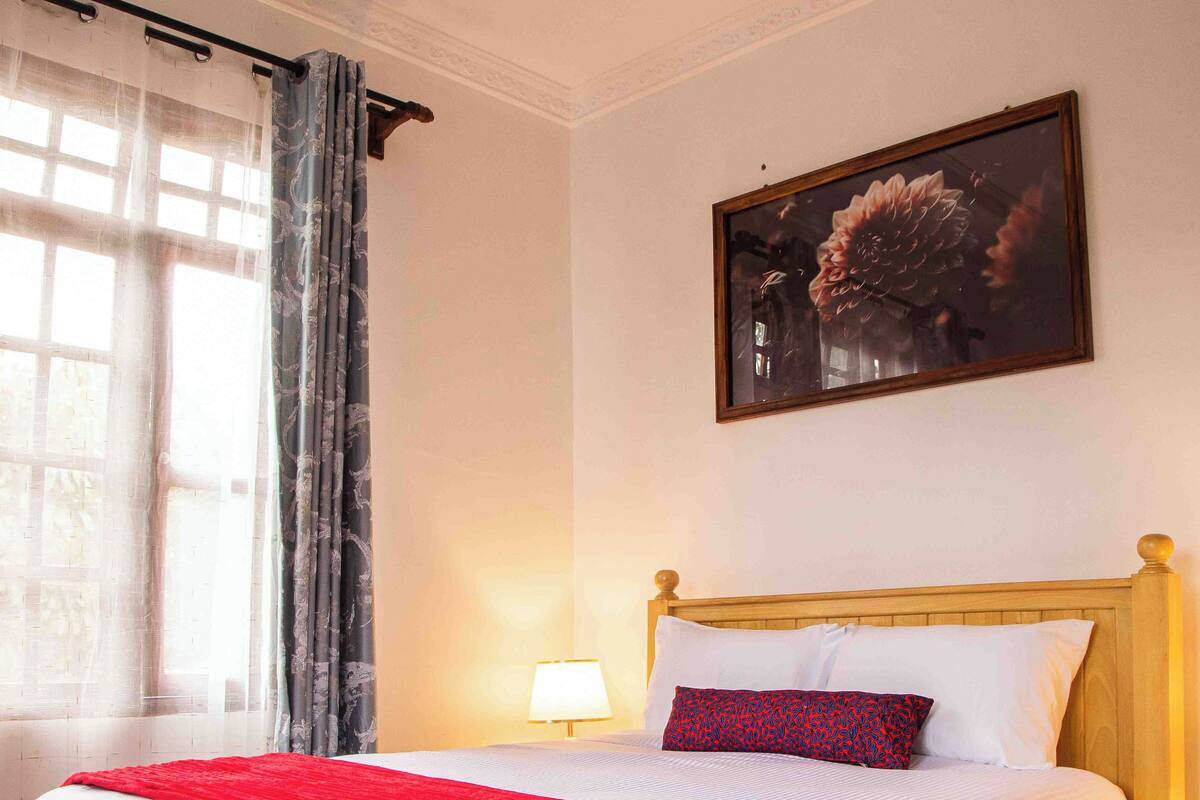 A neatly made bed with a wooden headboard, a red throw blanket, and a white comforter.