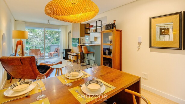 Un comedor con mesa de madera dispuesta para dos personas, una lámpara colgante de mimbre y vistas al exterior a través de grandes ventanales.