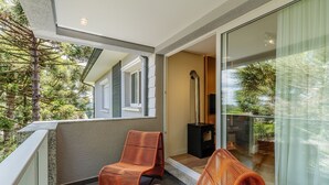 Un balcón con dos sillones de mimbre, una chimenea y un ventanal de vidrio que da a un jardín.
