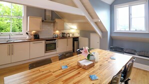 A modern kitchen with white cabinets, a wooden dining table, and a large window. - 2 The Old School House (Dartmouth)