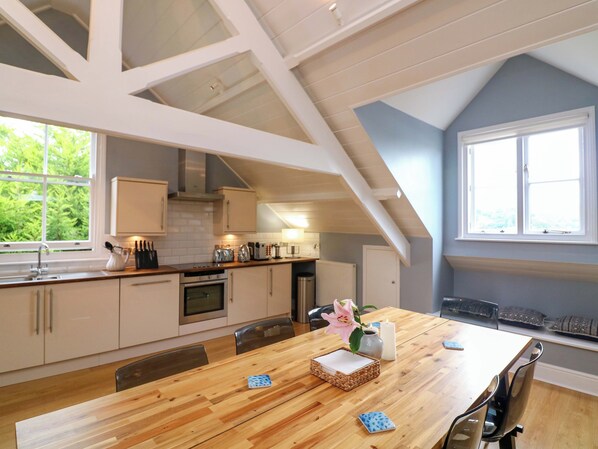 A modern kitchen with white cabinets, a wooden dining table, and a large window.