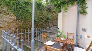 A patio with a wooden table and chairs, a metal fence, and a stone wall with greenery. - 2 The Old School House (Dartmouth)