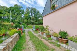 A garden pathway leading to a building with a pink exterior, surrounded by various potted plants and a small water feature.