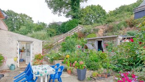 Un patio con una mesa y sillas, rodeado de macetas con plantas y flores.